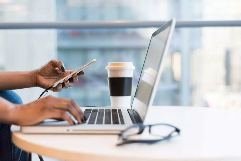 Person using a laptop with a coffee cup and smartphone on a table.